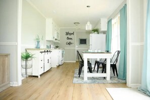 A modern kitchen with white cabinetry, a dining area with a table and chairs, and a wall with a 'Blessed love Coffee' sign. - Peaceful 3BR/2BA House Near EVERYTHING w/WIFI (Dothan)