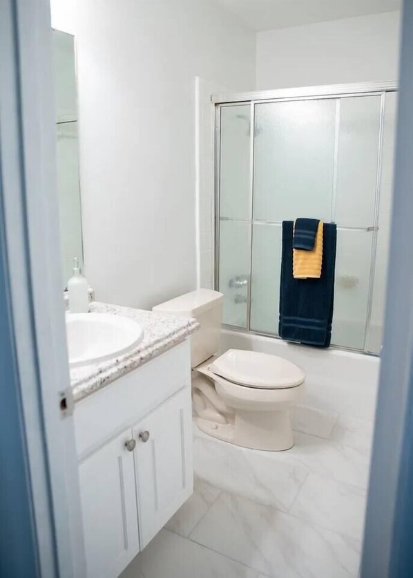 Et badeværelse med et hvidt toilet, en vask med marmorbordplade og en brusekabine i glas.