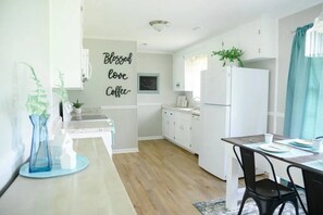 A modern kitchen with white cabinetry, a wooden countertop, a dining area with a table and chairs, and a wall with a 'Blessed love Coffee' sign. - Peaceful 3BR/2BA House Near EVERYTHING w/WIFI (Dothan)