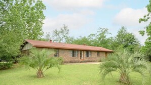 A single-story brick house with a red roof, surrounded by a well-maintained lawn and palm trees. - Peaceful 3BR/2BA House Near EVERYTHING w/WIFI  (Dothan)