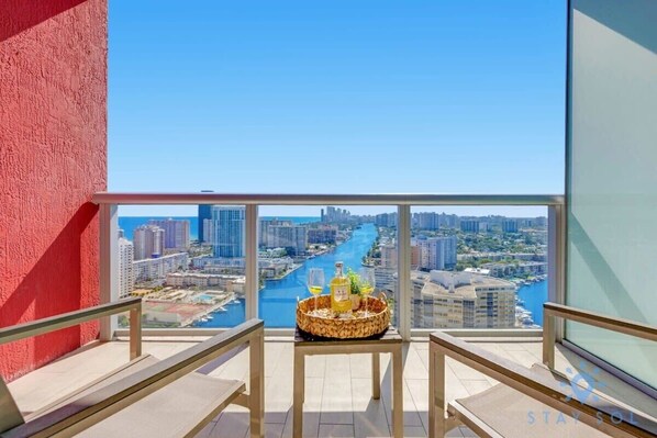 Un balcon avec vue sur la ville, un panier en osier rempli de boissons et un ciel dégagé.