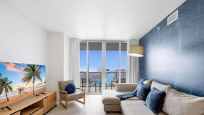 Ein modernes Wohnzimmer mit großem Fenster, einer Couch, einem Sessel, einem Fernseher und einem Balkon mit Stadtblick.