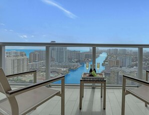 A balcony with a table, two chairs, and a view of a cityscape and water body. - Spacious 2 Bedroom + Sleeps 6 + Pool + Gym (Hallandale Beach)