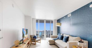 A modern living room with a large window, a sofa, a chair, a TV, and a decorative wall.