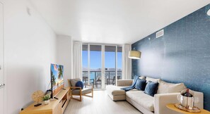 A modern living room with a large window, a sofa, a chair, a TV, and a decorative wall.