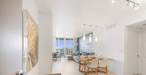 A modern living room with a dining area, large windows, and a view of the city. - Upper Apartment + Pool + Gym + Amazing view (Hallandale Beach)