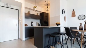 Una cocina moderna con armarios oscuros, una isla central, taburetes negros y una mesa de comedor con sillas.