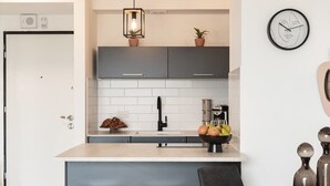 Una cocina moderna con armarios grises, encimera blanca, lámpara colgante, un reloj y un bol de fruta.
