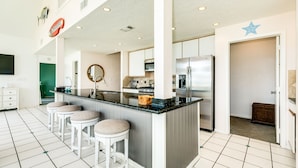Una cocina amplia con una isla central, taburetes de bar, un refrigerador y un microondas.