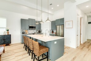 A modern kitchen with grey cabinets, a large island with bar stools, and pendant lighting.