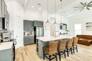 A modern kitchen with grey cabinets, a central island with bar stools, stainless steel appliances, pendant lighting, and a ceiling fan.