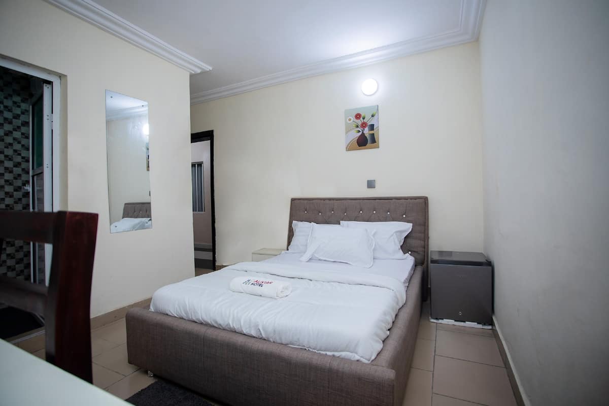 A neatly made bed with white linens, a bedside table with a lamp, and a small bedside heater.