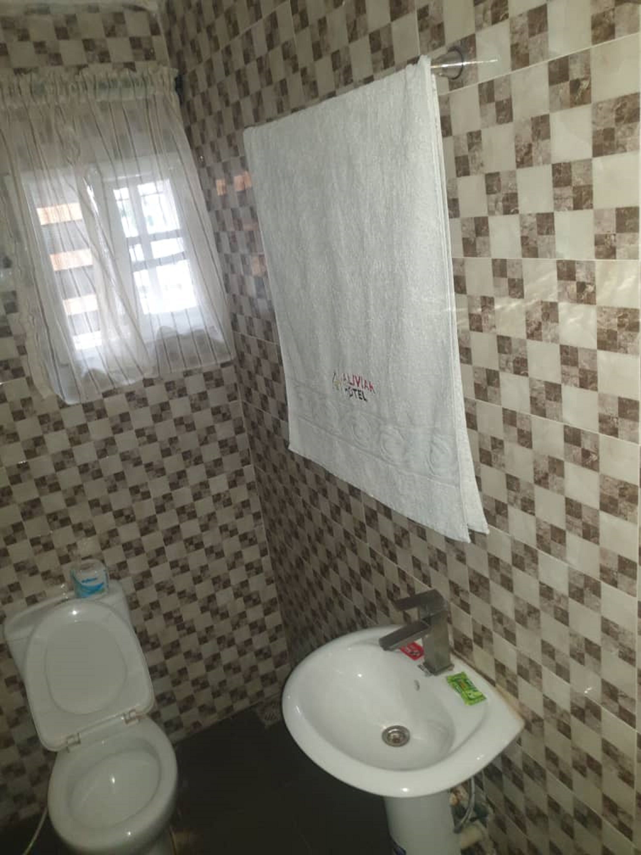 A bathroom with a checkered tile wall, a toilet, a sink, and a towel hanging on the wall.