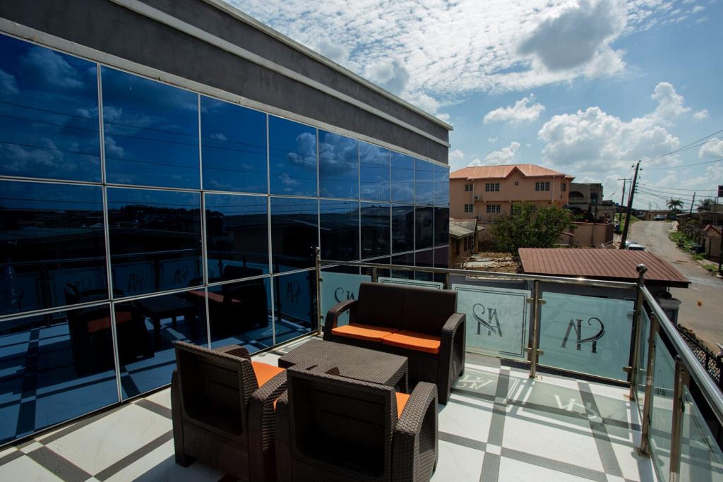 A balcony with wicker furniture and a glass wall reflecting the sky and buildings.