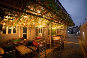 An outdoor seating area with wooden benches and tables, covered by a roof with hanging plants and string lights. - ALIVIAR HOTEL IBADAN (Ibadan)