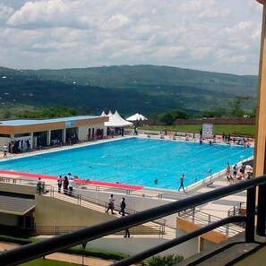 A swimming pool with people around it, a white tent, and a building in the background. - HOTEL LA PALISSE NYAMATA  (Ntarama)
