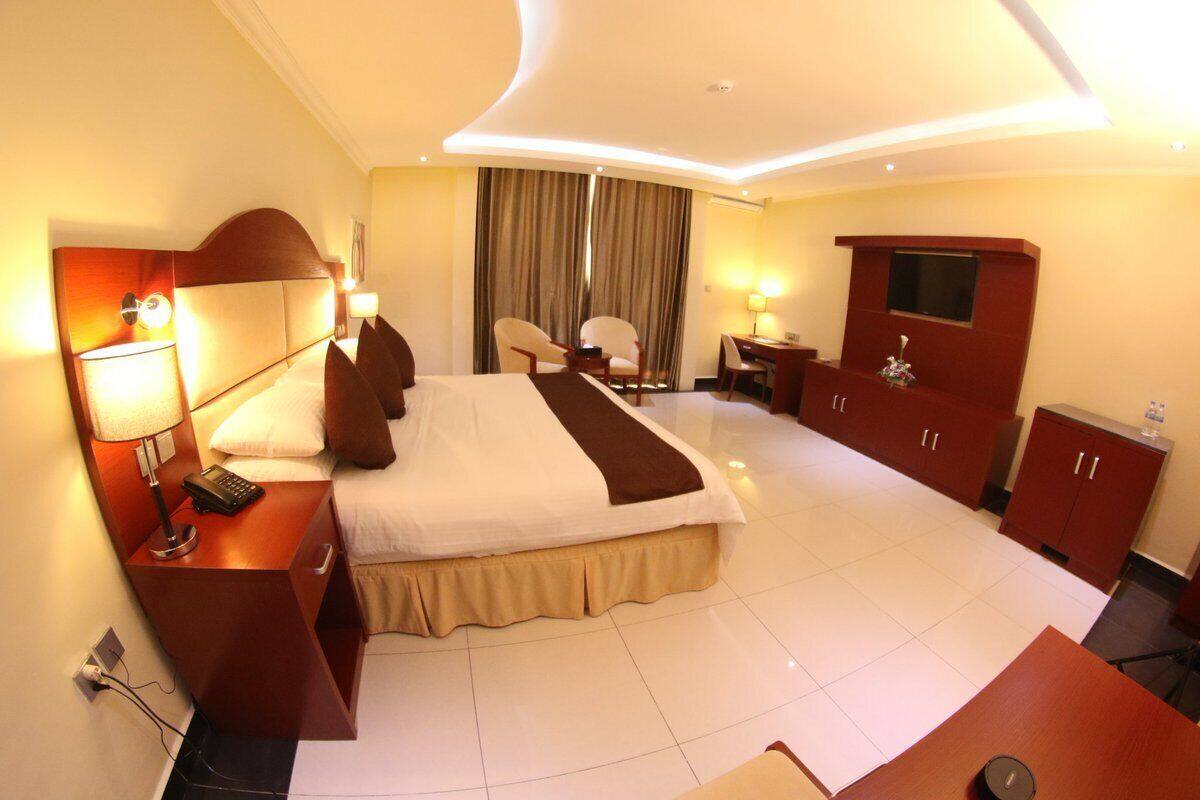 A hotel room with a large bed, bedside tables, a desk, a TV, and a wardrobe.