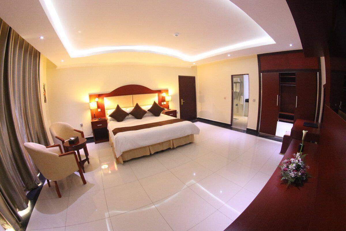 A modern hotel room with a large bed, a sitting area with a chair and a small table, and a large mirror.