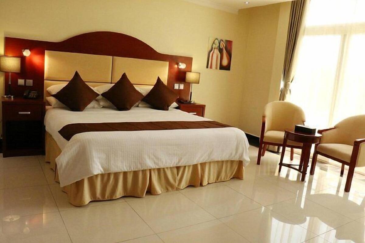 A hotel room with a large bed, two bedside tables, a chair, and a painting on the wall.