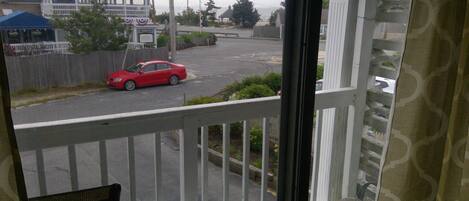 Uitzicht vanaf een balkon, met een rode auto in de straat, een blauwe tent en een gebouw met een wit hek.