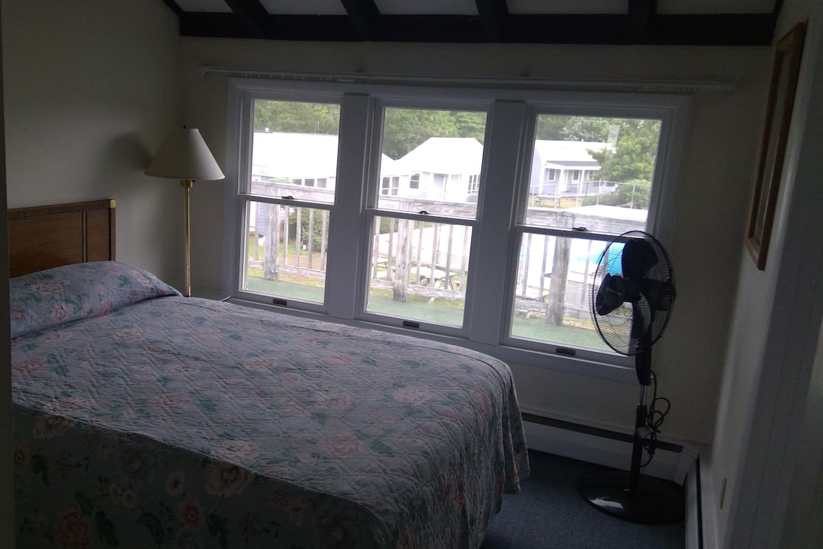 Une chambre à coucher avec un lit, une fenêtre et un ventilateur sur pied.
