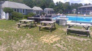 Un jardin avec des tables de pique-nique, un barbecue et une piscine.