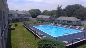 Une piscine avec des chaises longues, une terrasse clôturée et un espace herbeux équipé de tables de pique-nique.