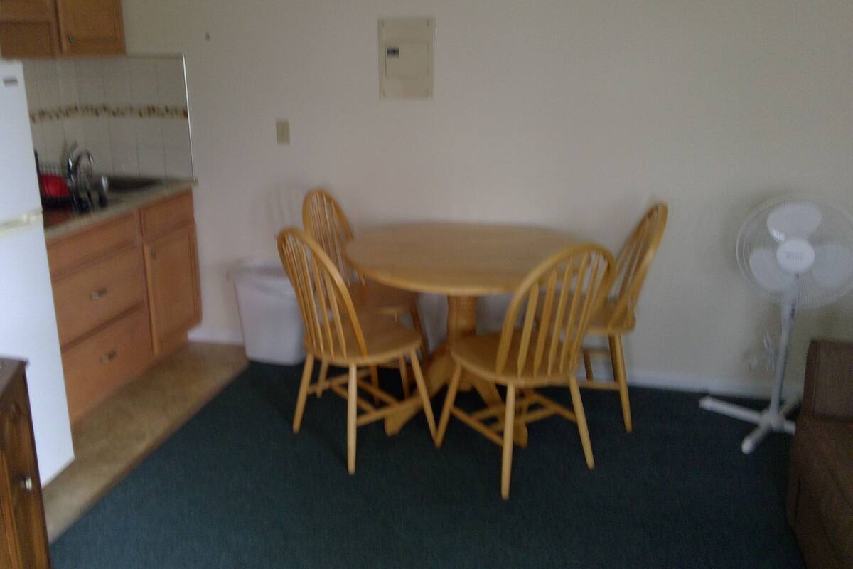 Une cuisine compacte comprenant une table et des chaises, un réfrigérateur et un petit ventilateur.