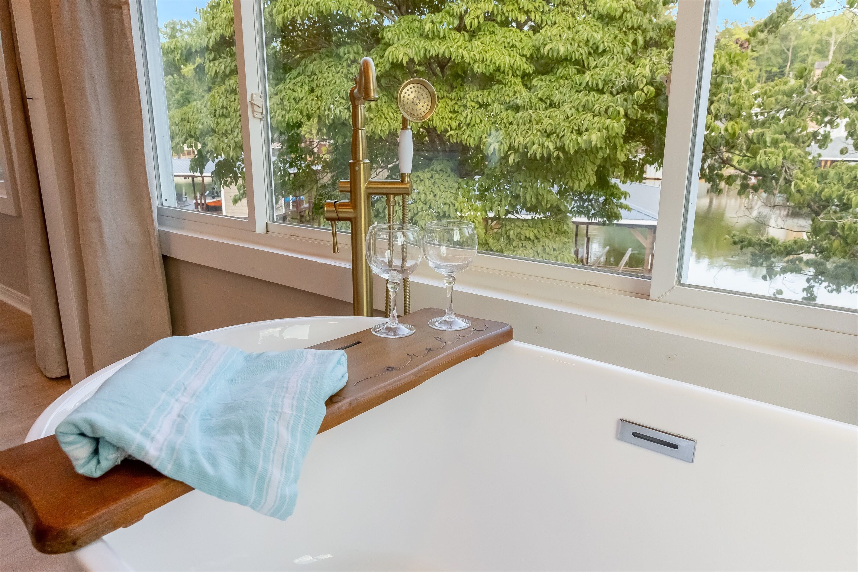 Une baignoire avec un plateau en bois sur lequel sont posés deux verres et un pommeau de douche.
