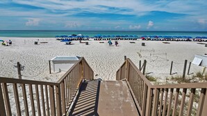 A beach with a wooden staircase leading down to the sand, a row of blue umbrellas, and a clear view of the ocean. - 🏖️XL Balcony with Awesome View - 2BR Boardwalk 209C🏖️ (Panama City Beach)