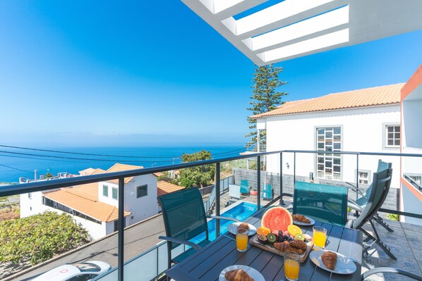 A balcony with a pool, dining table, and breakfast items. - Casa Teixeira by Atlantic Holiday (Calheta)