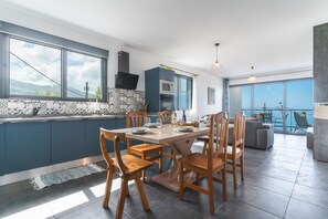 A modern kitchen with a large island, blue cabinetry, and a view of the sea. - Casa Teixeira by Atlantic Holiday (Calheta)