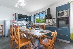 A modern kitchen with a dining table set for four, wooden chairs, a built-in oven, and a window with a mountain view.