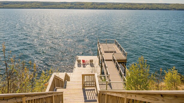 A wooden dock leading to a lake with a clear view of the water and distant trees. - Spacious Finger Lakes Waterfront Lodge (Road Burdett)