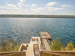 A wooden dock leading to a lake with a clear view of the water and distant trees. - Spacious Finger Lakes Waterfront Lodge (Road Burdett)