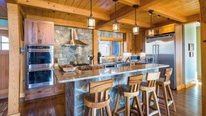 A spacious kitchen with wooden beams, stone accents, stainless steel appliances, and a large island with bar stools. - Spacious Finger Lakes Waterfront Lodge (Road Burdett)