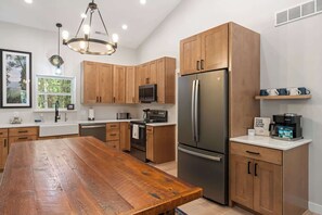 A modern kitchen with wooden cabinets, a stainless steel refrigerator, a built-in microwave, and a wooden dining table.