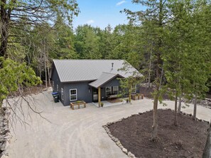A modern house with a metal roof, surrounded by trees and a gravel driveway. - Relax at Newly Constructed home in Egg Harbor (Egg Harbor)
