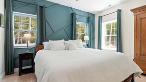 Une chambre à coucher comprenant un lit, des tables de chevet, une fenêtre avec des rideaux et une armoire en bois.