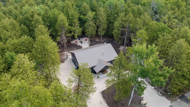 Une vue aérienne d’une maison entourée d’une forêt dense, avec un patio bien visible et un grand toit.