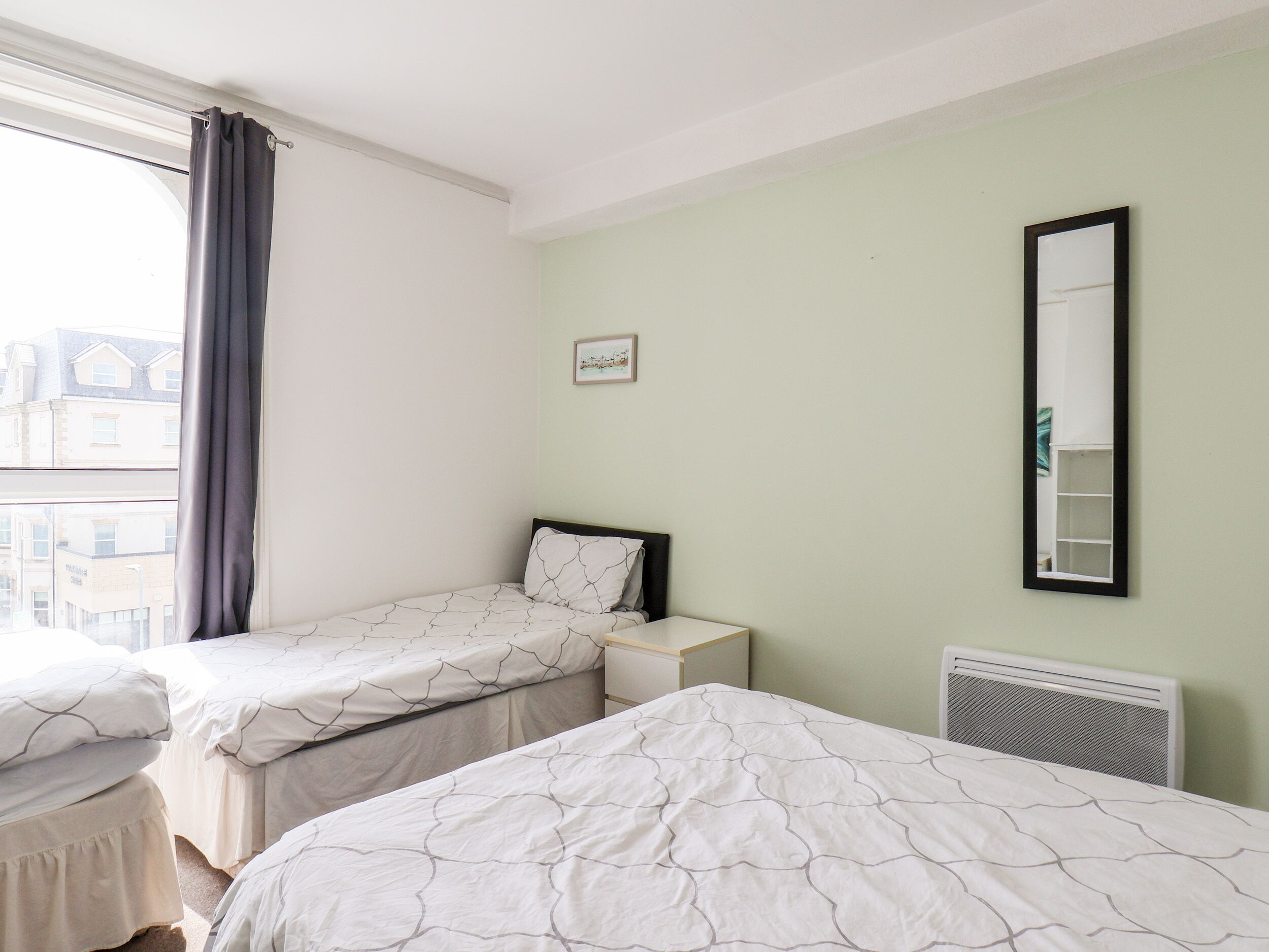 Ein Zimmer mit zwei Einzelbetten, einem Nachttisch, einem Spiegel und einer Heizung.