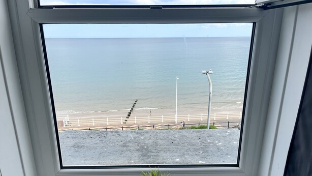 Ein Fenster mit Blick auf einen Strand, einem weißen Geländer und einem Blumentopf auf dem Fensterbrett.