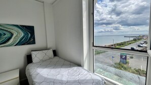 Ein Schlafzimmer mit einem Bett, einem Fenster mit Meer- und Straßenblick sowie einem Bild an der Wand.