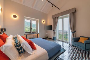 A hotel room with a bed, a sofa, a TV, a balcony with curtains, and a view of the outdoors.