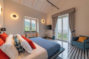 A hotel room with a bed, a sofa, a TV, a balcony with curtains, and a view of the outdoors.