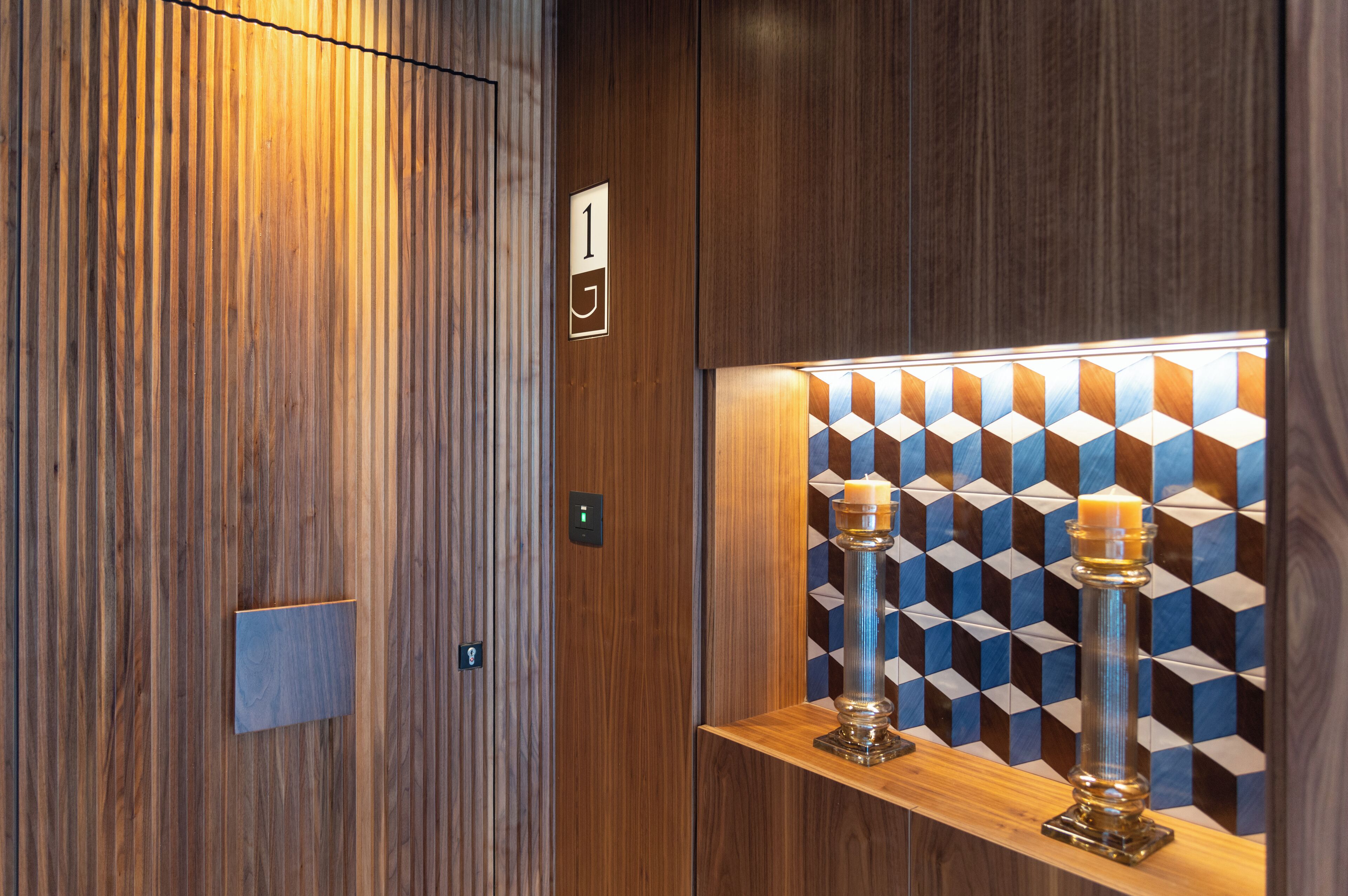 An elevator interior with a wooden finish, a number 1 sign, and a geometric patterned wall.