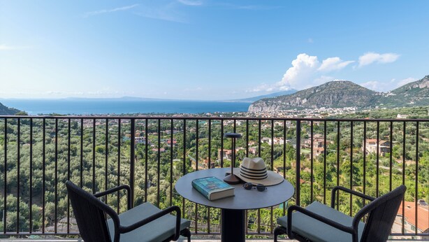 A balcony with a table, two chairs, a book, a hat, and sunglasses. - Gargiulo Resort (Sant'Agnello)