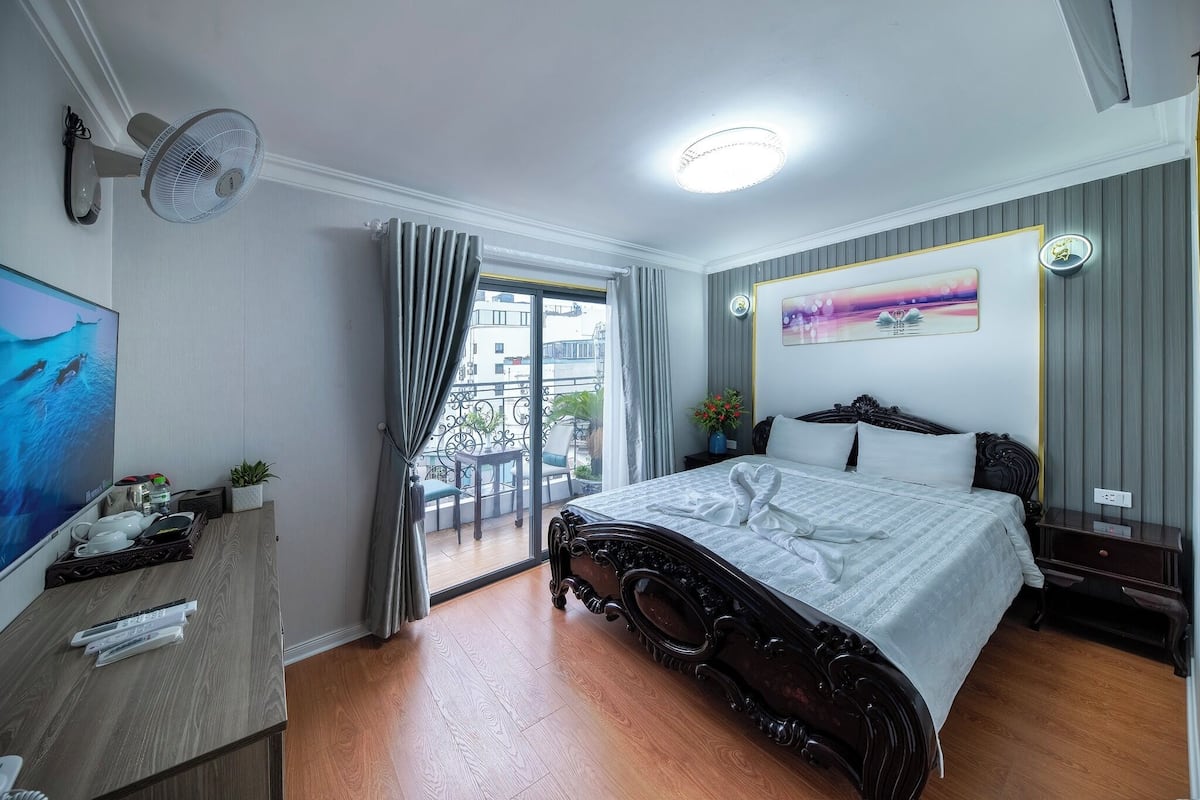A hotel room with a bed, a desk, a TV, a balcony with a view, and a ceiling fan.