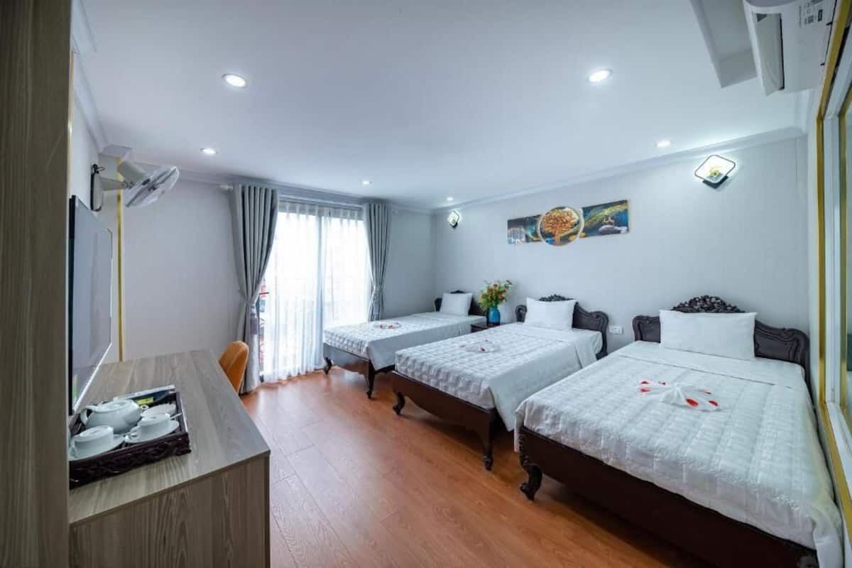 A hotel room with two single beds, a desk with a tray of cups, a chair, and a window with curtains.