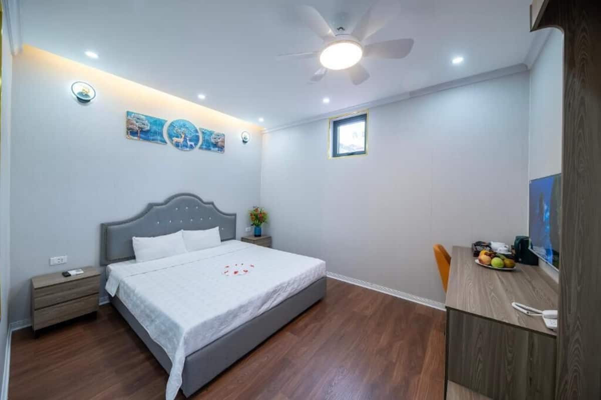 A bedroom with a bed, bedside table, nightstand, desk, chair, and a small window.